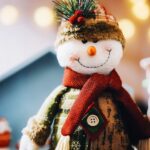 Photo of toy snowman plush wearing scarf and woolly hat with pine bow on it